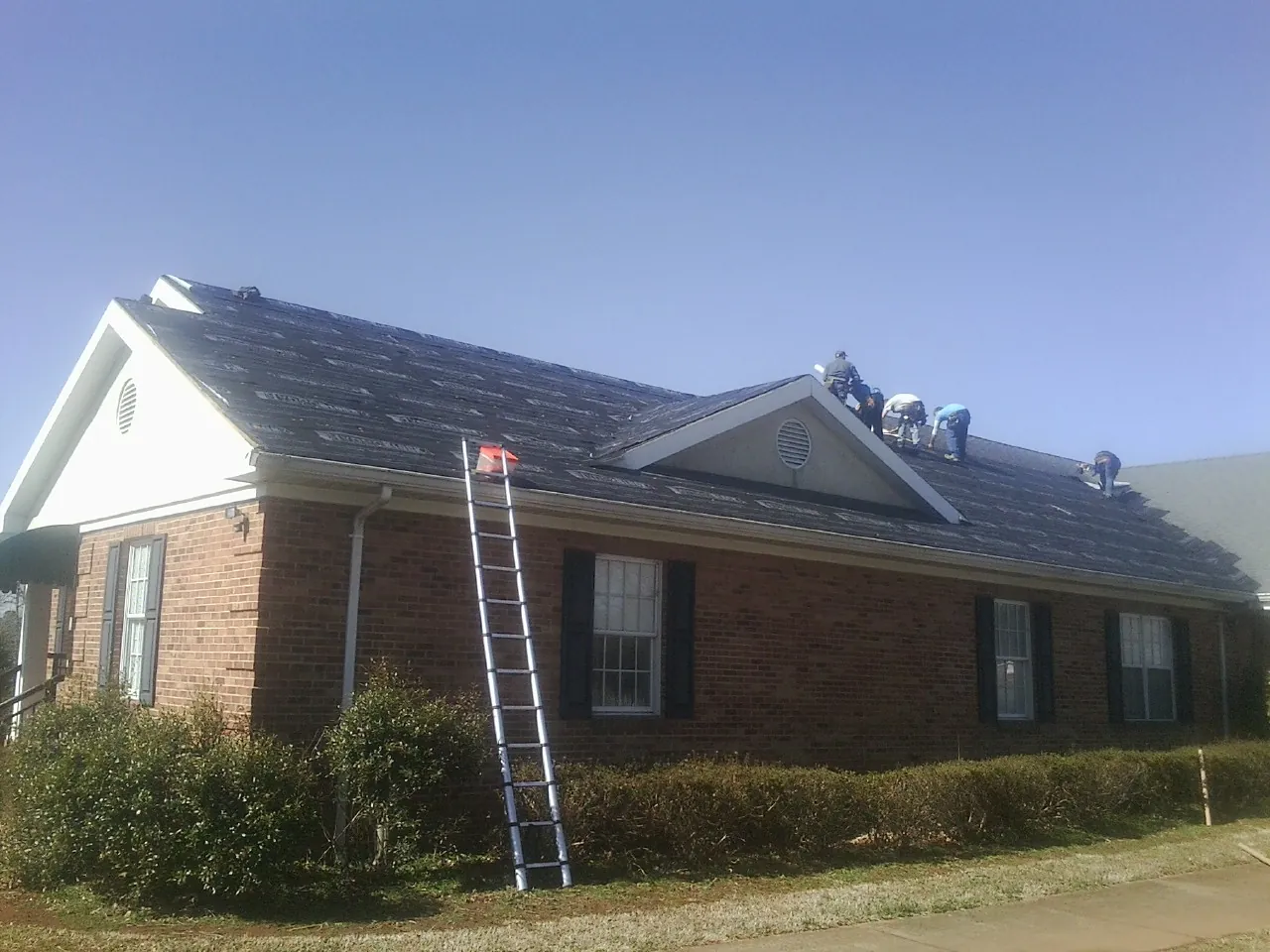Crew tearing shingles off a brick ranch roof with a ladder set — Metal Roof Repair work by our crew in Pine Hill