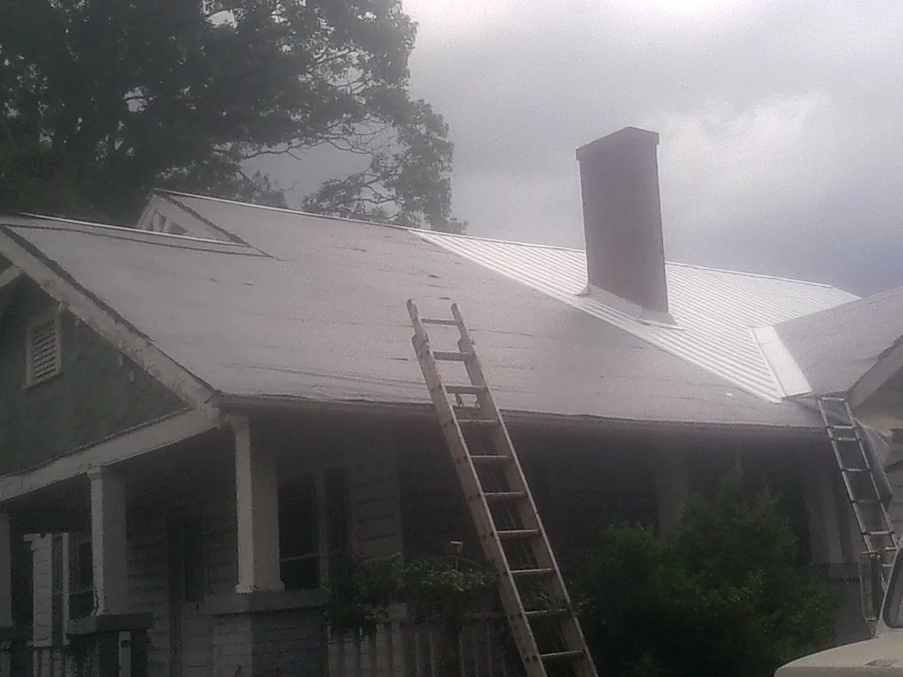 Ladders against a metal roof on an older home with a brick chimney in Pine Hill