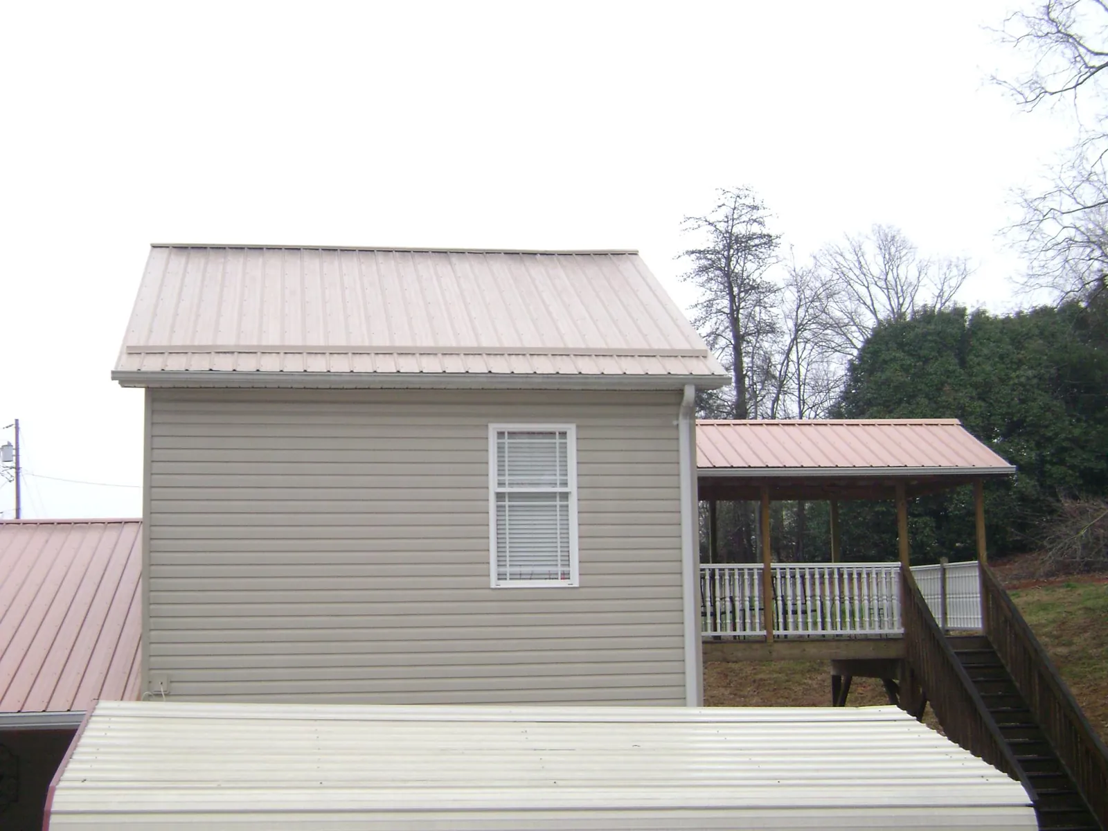 Tan metal roofs on a two story addition and attached porch, from a Roof Replacement job in Pine Hill